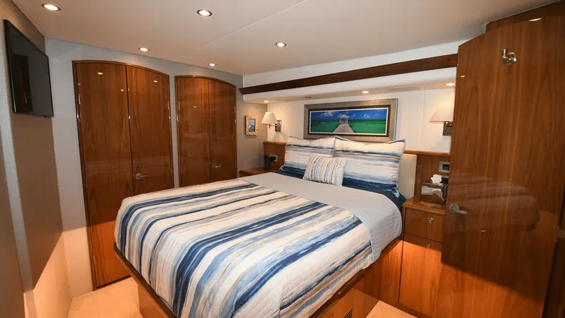 Slide: The Image of Master Stateroom with Queen Bed The master stateroom of the 2020 Viking 58 Convertible features a luxurious queen-sized bed adorned with striped bedding. Rich wood finishes create a warm and inviting atmosphere, complemented by ample storage with elegantly crafted cabinets. Recessed lig - 6388289