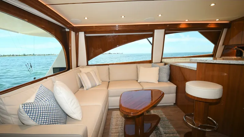 Slide: The Image of Spacious Salon with Ocean View This inviting salon on the 2020 Viking 58 Convertible features a plush L-shaped sofa complemented by elegant wood finishes and large windows offering panoramic ocean views. The space is enhanced by recessed lighting, adding a warm ambiance, while the styl - 6388292