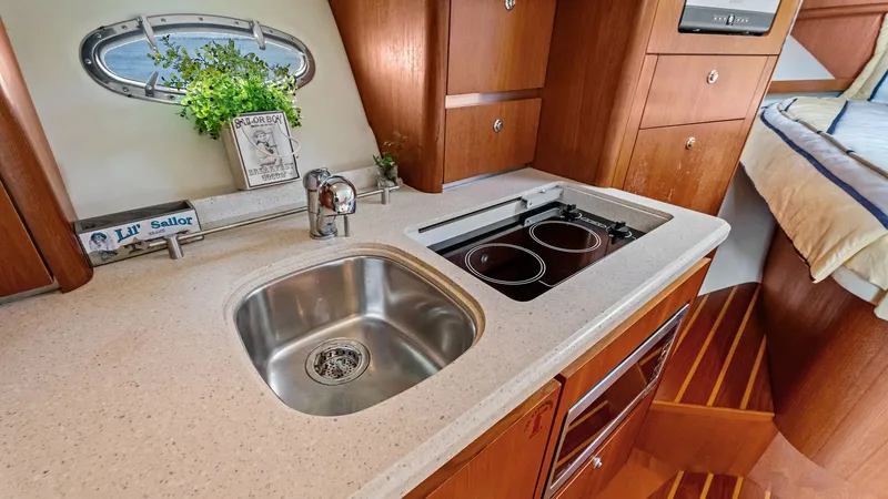 Slide: The Image of Galley with Sink and Stove This well-appointed galley features a sleek stainless steel sink and a dual-burner stove, perfect for meal preparation at sea. The warm wood cabinetry provides ample storage space, complemented by elegant countertops. A small porthole window adds natural - 6394578