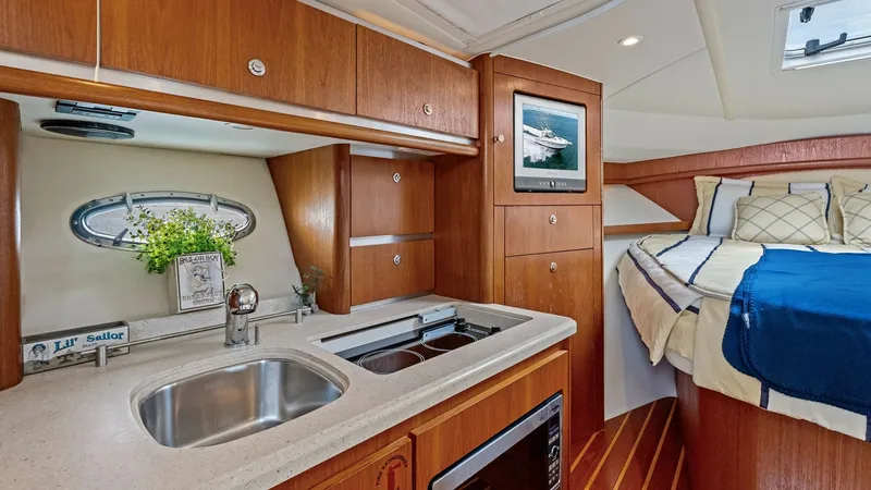 Slide: The Image of Galley and Forward Berth Area This cozy interior of the 2007 Tiara Yachts 32 Open features a well-appointed galley with a sleek sink, two-burner stove, and microwave. The warm wood cabinetry provides ample storage, while the nearby forward berth offers a comfortable sleeping area ador - 6394579