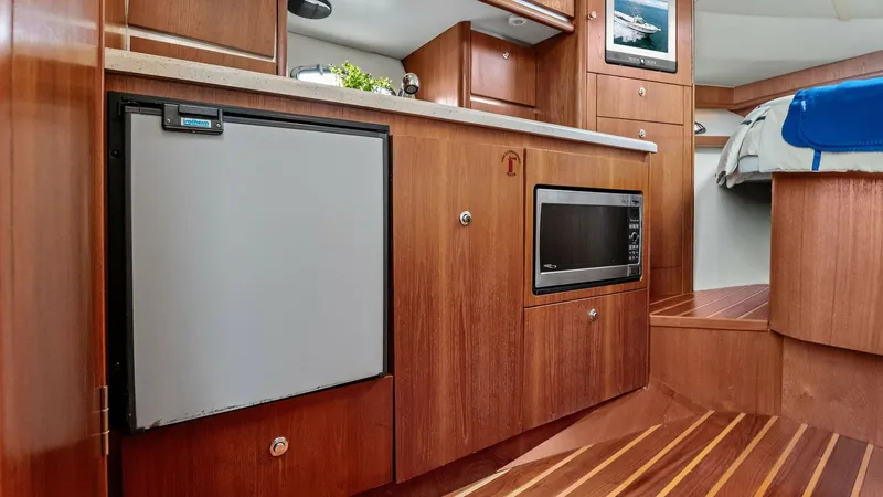 Slide: The Image of Galley with Modern Appliances This inviting galley on the 2007 Tiara Yachts 32 Open features sleek wood cabinetry and rich flooring, providing a warm and functional space. Equipped with a compact refrigerator and a built-in microwave, it offers all the essentials for meal preparation. - 6394574