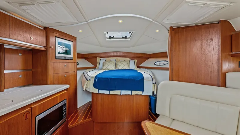 Slide: The Image of Luxurious Forward Cabin View This inviting forward cabin on the 2007 Tiara Yachts 32 Open showcases a spacious berth with elegant wood finishes and plush bedding. The cabin is well-lit with integrated ceiling lights and a skylight, enhancing the warm and cozy atmosphere. Ample storag - 6394577