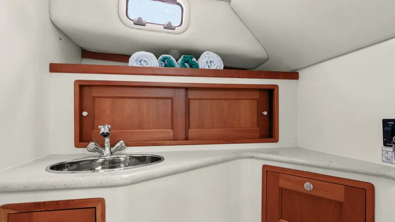 Slide: The Image of Compact Yacht Head with Storage This well-appointed yacht head features a sleek, stainless steel sink set into a smooth, light-colored countertop. The warm wood cabinetry provides ample storage space, enhancing the room's functionality and aesthetic appeal. A small porthole allows natur - 6479424