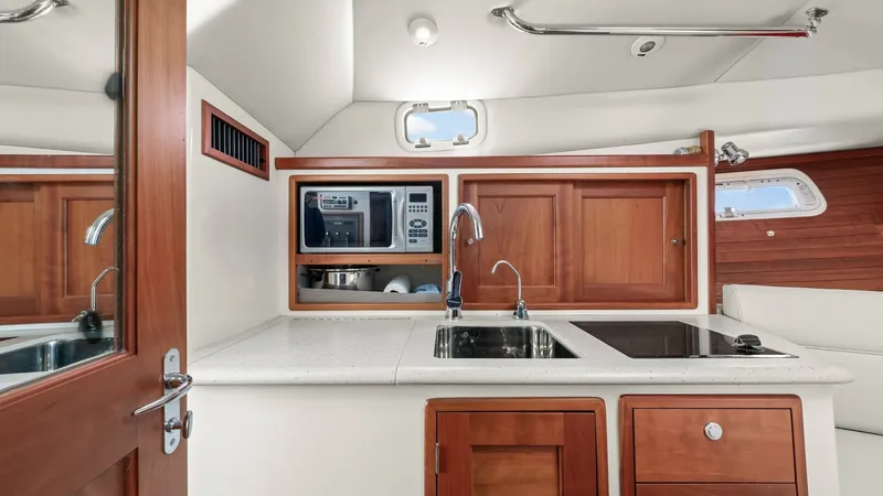 Slide: The Image of Galley with Dual Sink and Appliances The well-appointed galley of the 2008 MJM Yachts 29z features a sleek dual sink setup with a modern faucet, complemented by a built-in microwave and ample storage cabinets. The polished wooden cabinetry adds warmth and elegance, while the compact cooktop - 6479414