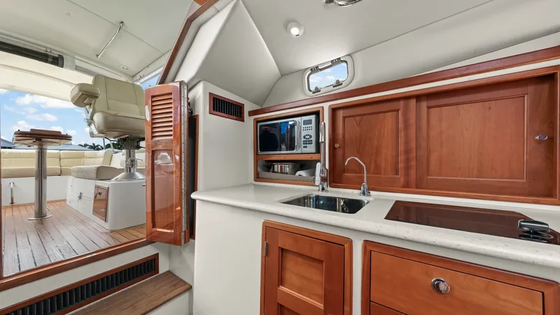 Slide: The Image of Galley and Cockpit Transition This image showcases the well-appointed galley of the 2008 MJM 29z, featuring rich wood cabinetry and modern appliances, including a built-in microwave and sleek sink. The design facilitates easy transition to the cockpit area, which offers comfortable se - 6479411