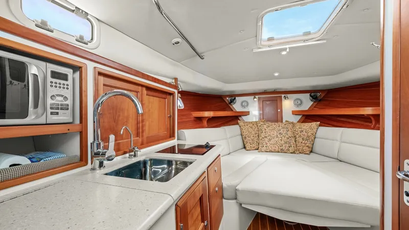 Slide: The Image of Elegant Interior Galley and Lounge The interior of the 2008 MJM Yachts 29z features a sophisticated galley and lounge area. The galley is equipped with a modern sink and microwave, set against rich wooden cabinetry. The plush seating area offers comfort and style, with ample natural light - 6479417