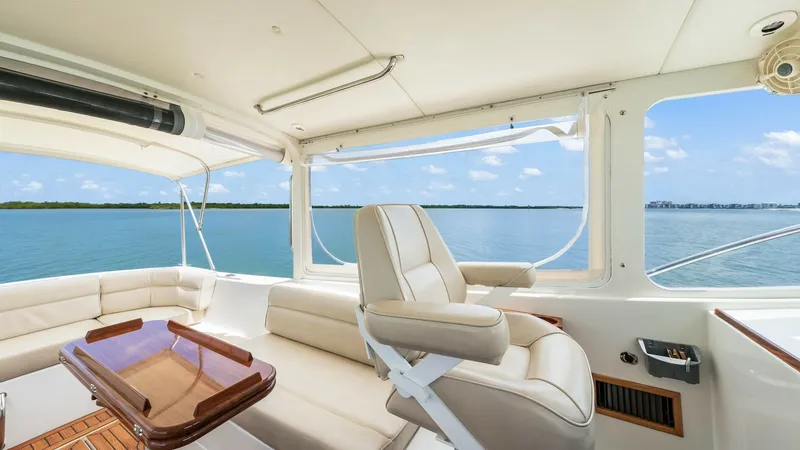 Slide: The Image of Spacious Helm and Seating Area This image showcases the helm and seating area of the 2008 MJM Yachts 29z Camelot. The helm features a plush captain's chair and a sleek wooden table, surrounded by large windows offering panoramic views of the water. Light-colored upholstery and teak flo - 6479390