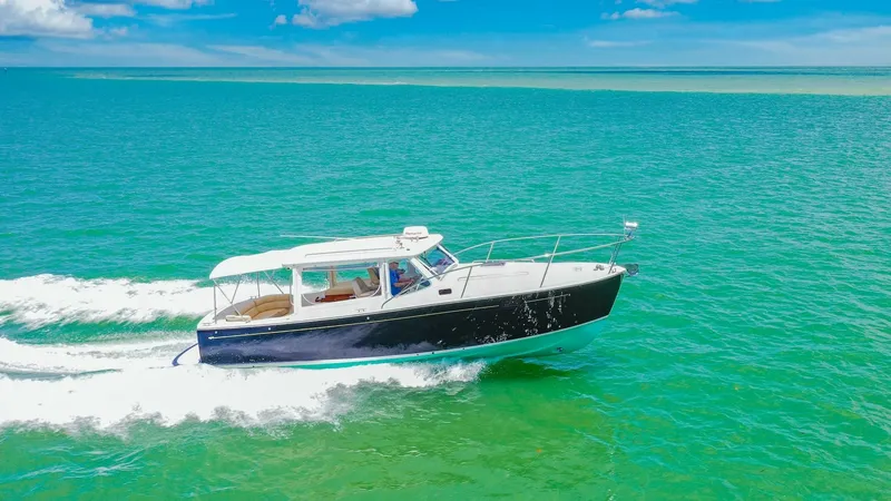 Slide: The Image of Side View Cruising on Open Water The MJM Yachts 29z 'Camelot' glides effortlessly through vibrant turquoise waters, showcasing its sleek, classic design. The vessel's deep blue hull contrasts beautifully with the white superstructure, emphasizing its elegant lines. The spacious cockpit a - 6479434