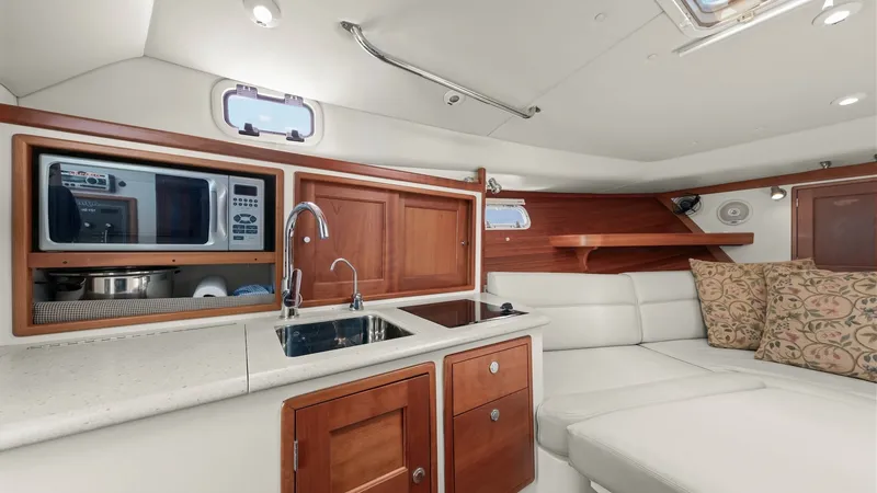 Slide: The Image of Galley and Lounge Area Interior This inviting interior features a compact galley with warm wood cabinetry and a sleek countertop, complete with a stainless steel sink and built-in microwave. Adjacent to the galley, the cozy lounge area offers plush white seating, accented by patterned c - 6479415