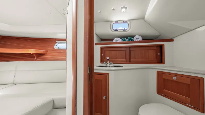 Slide: The Image of Compact Cabin with Ensuite Head This image showcases the cozy cabin of the MJM 29z, featuring a well-appointed ensuite head. The space is adorned with rich wood cabinetry, offering ample storage and a sophisticated touch. The sleek design and efficient layout maximize comfort and functi - 6479421