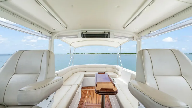 Slide: The Image of Spacious Cockpit Seating Area This image showcases the inviting cockpit of the 2008 MJM Yachts 29z. The area features plush, cream-colored seating with a sleek wooden table centerpiece, offering a perfect setting for relaxation or entertaining. Surrounded by large windows, the space i - 6479389