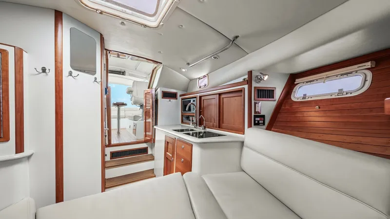 Slide: The Image of Galley and Salon Interior View The interior of the MJM Yachts 29z showcases a well-appointed galley with rich wood cabinetry and a sleek countertop. The adjacent salon area features plush seating, offering a comfortable space for relaxation. Natural light pours in through the overhead - 6479410