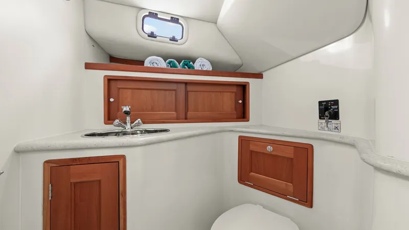 Slide: The Image of Compact Yacht Head with Storage This well-appointed head on the MJM 29z features a sleek, modern design with practical amenities. The space includes a compact sink with a polished faucet and ample countertop. Rich wooden cabinetry provides convenient storage, while the overhead porthole - 6479423