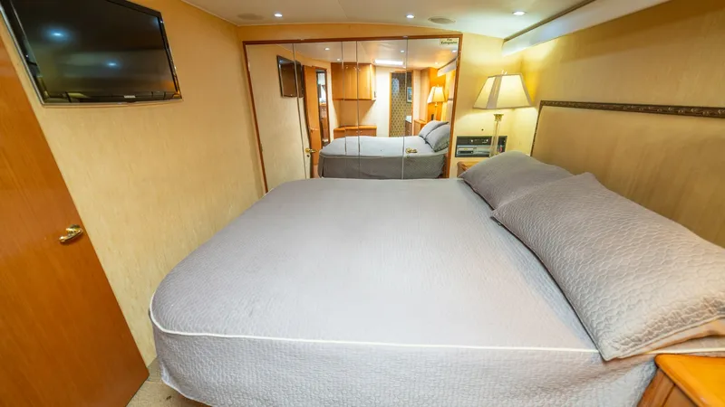 Slide: The Image of Master Stateroom 2002 Viking 61 Convertible The master stateroom offers a comfortable and inviting space, featuring a large, plush bed with elegant bedding. The room is enhanced by warm wood finishes and soft ambient lighting, creating a relaxing atmosphere. A mirrored wall adds depth, while a moun - 6683632