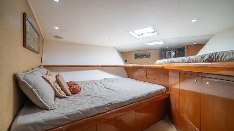 Slide: The Image of Forward VIP Stateroom 2002 Viking 61 Convertible This inviting forward stateroom features a cozy, queen-sized berth with plush bedding, perfect for restful nights at sea. The rich wood cabinetry provides ample storage, complementing the warm tones of the room. A skylight and recessed lighting brighten t - 6683637