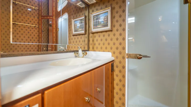 Slide: The Image of Master Bathroom with Shower 2002 Viking 61 Convertible This sophisticated bathroom on the Viking 61 Convertible features a sleek vanity with a polished countertop and elegant fixtures. The warm wood cabinetry complements the classic wallpaper, creating a luxurious ambiance. A spacious shower with a glass door - 6683633