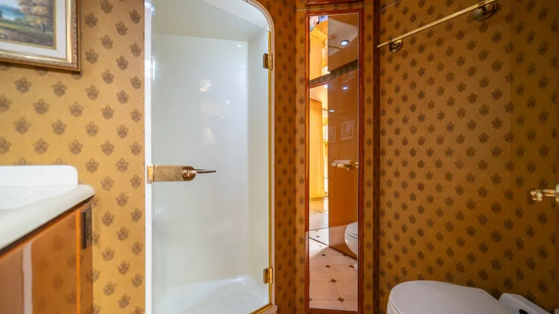 Slide: The Image of Master Bathroom with Shower 2002 Viking 61 Convertible This luxurious bathroom on the 2002 Viking 61 Convertible features a spacious enclosed shower, accented by gold hardware for a touch of elegance. The rich, patterned wallpaper and mirrored storage create a sophisticated ambiance, while the pristine white - 6683634