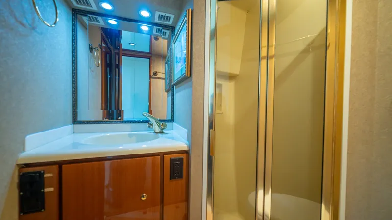 Slide: The Image of Ensuite Bathroom with Vanity and Shower 2002 Viking 61 Convertible This elegant ensuite bathroom on the Viking 61 Convertible features a sleek vanity with a polished countertop and ample storage. The space is well-lit with recessed lighting, enhancing the warm wood cabinetry. Adjacent is a glass-enclosed shower, providin - 6683627