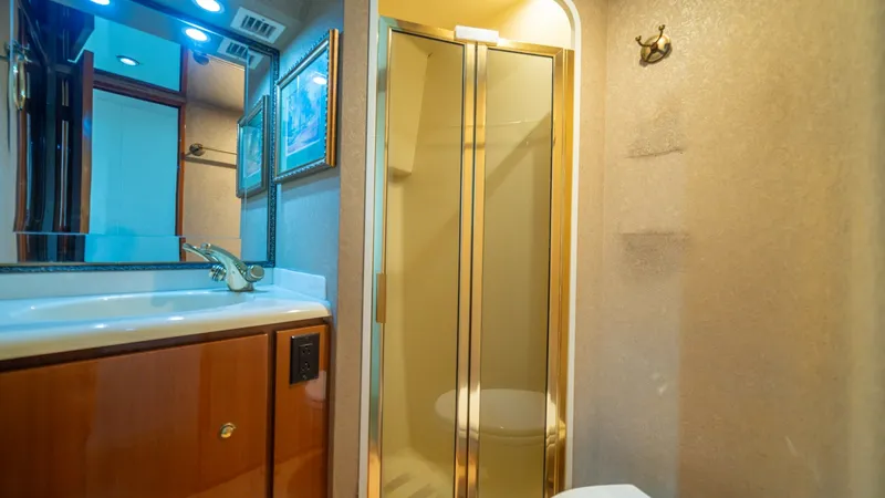 Slide: The Image of Guest Stateroom Head 2002 Viking 61 Convertible This well-appointed head compartment features a sleek vanity with integrated sink and polished fixtures. The shower enclosure is elegantly designed with a glass door, providing both functionality and style. Warm wood cabinetry and soft lighting create a c - 6683628