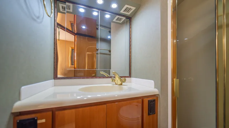 Slide: The Image of Forward VIP Head2002 Viking 61 Convertible This image showcases the elegant vanity area within the ensuite head of the 2002 Viking 61 Convertible. Featuring a polished wood finish, the vanity is complemented by a sleek, integrated sink and gold-toned fixtures. Above, the mirrored cabinet is illumi - 6683642