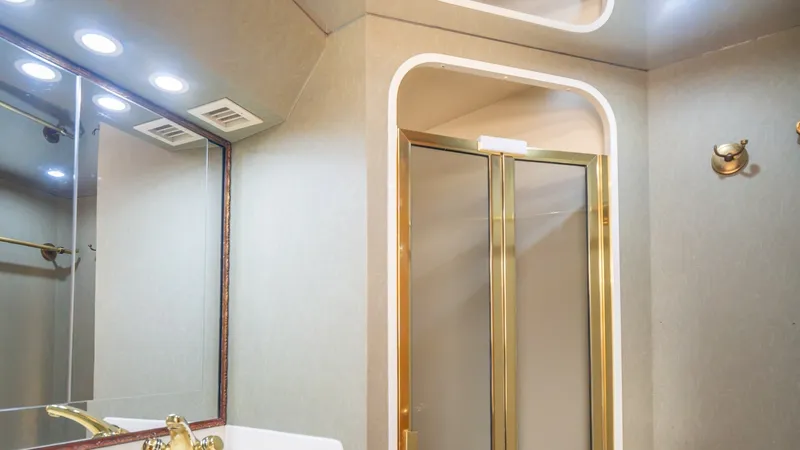 Slide: The Image of Forward VIP Head Viking 61 Convertible This refined ensuite bathroom on the 2002 Viking 61 Convertible features elegant gold fixtures and a spacious glass-enclosed shower. The well-lit vanity area is complemented by ample mirror space, providing a sense of openness and luxury. The warm, neutra - 6683641
