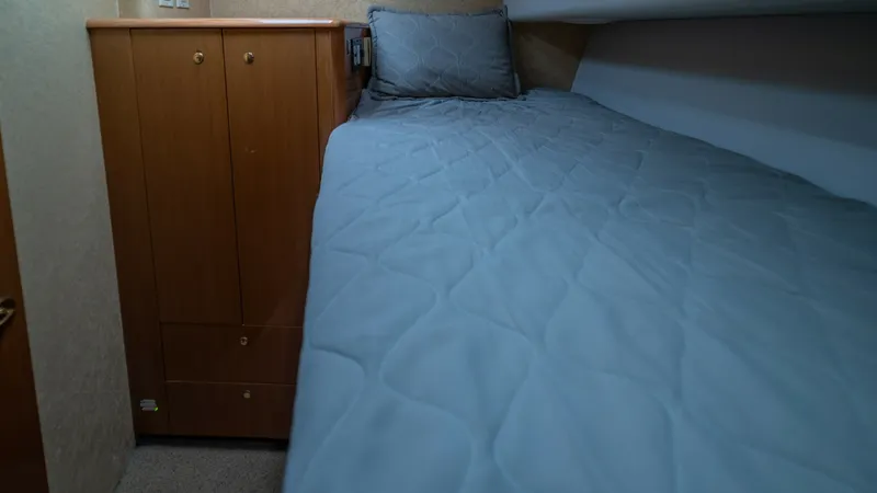 Slide: The Image of Guest Stateroom with Single Berth 2002 Viking 61 Convertible This cozy guest stateroom features a comfortable single berth adorned with a soft, quilted bedspread. The warm wood cabinetry offers practical storage space, complementing the room's inviting ambiance. Soft lighting and neutral tones create a serene envir - 6683625