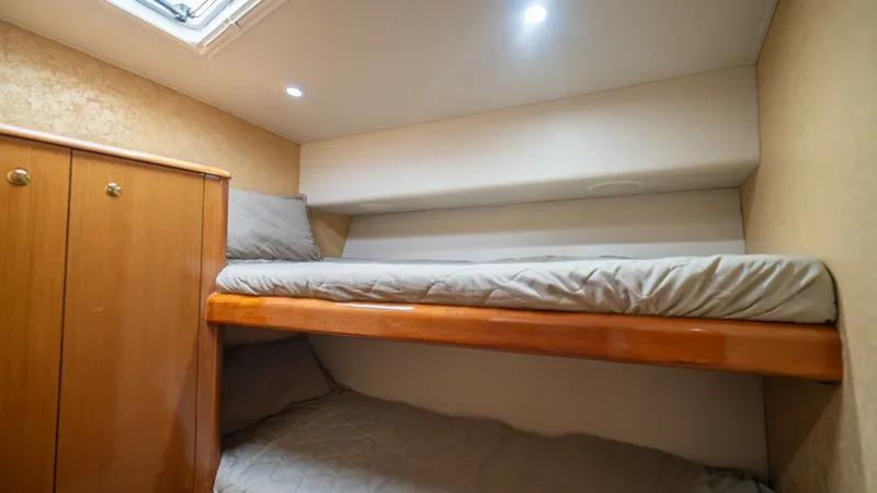 Slide: The Image of Guest Cabin with Bunk Beds 2002 Viking 61 Convertible  This cozy guest cabin features stacked bunk beds with sleek wooden frames, providing a comfortable sleeping arrangement. The warm wood cabinetry offers ample storage space, complemented by soft ambient lighting from recessed fixtures. A skylight above all - 6683624