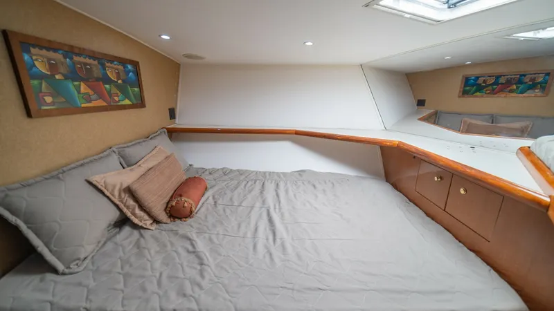 Slide: The Image of Forward VIP Stateroom 2002 Viking 61 Convertible This inviting forward stateroom features a spacious berth with plush bedding, creating a comfortable sleeping environment. The natural light from the overhead skylight enhances the warm tones of the wood accents and cabinetry, adding to the room's cozy am - 6683639