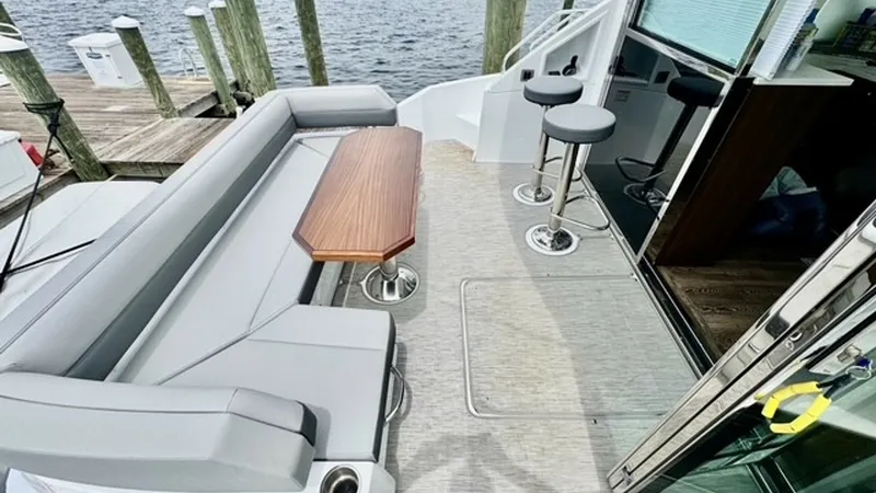 Slide: The Image of Aft Deck with Seating Area The aft deck of the 2023 Cruisers Yachts 50 Cantius features a spacious seating area with plush, modern cushions and a sleek wooden table, perfect for social gatherings. Adjacent to the seating, two stylish bar stools provide additional seating options. T - 6489157