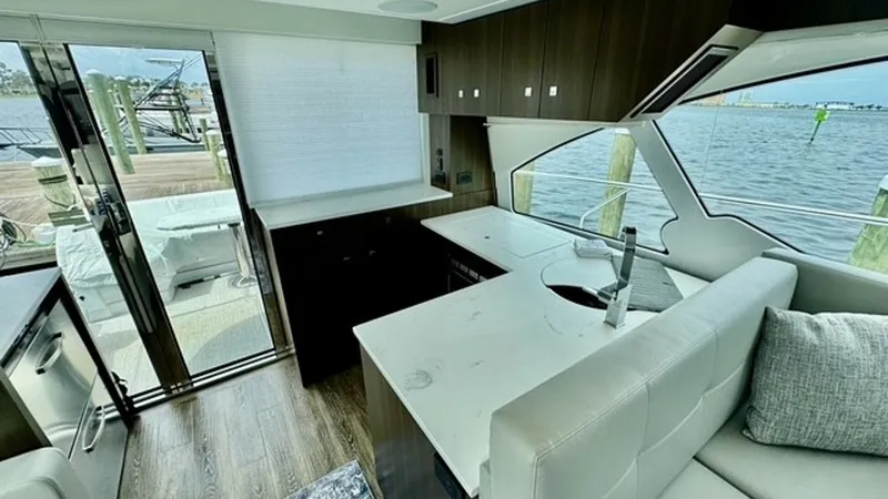 Slide: The Image of Galley and Salon Area with Water View The modern galley of the 2023 Cruisers Yachts 50 Cantius features sleek countertops and high-end appliances, seamlessly integrating with a comfortable salon area. Large windows and a sliding glass door provide ample natural light and stunning views of the - 6489140