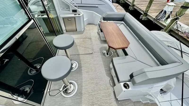 Slide: The Image of Spacious Aft Deck with Seating This inviting aft deck on the 2023 Cruisers Yachts 50 Cantius features elegant, cushioned seating surrounding a stylish wooden table, perfect for socializing and relaxation. The area includes sleek bar stools for additional seating, complemented by a comp - 6489134