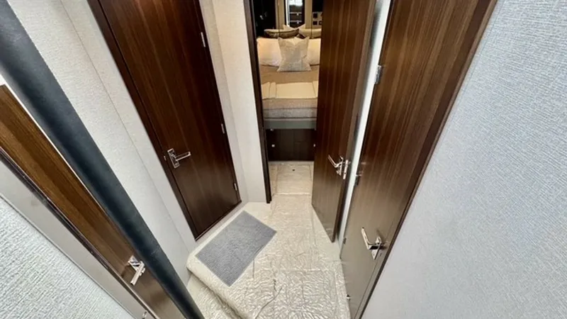 Slide: The Image of Lower Deck Hallway and Stateroom Entry This image showcases the elegantly designed lower deck hallway of the Cruisers Yachts 50 Cantius. The space is adorned with rich wood finishes on the doors, creating a warm and inviting atmosphere. The hallway leads towards the stateroom, offering a glimp - 6489148