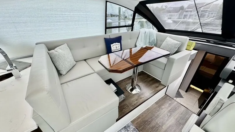 Slide: The Image of Main Salon Seating Area This inviting main salon on the 2023 Cruisers Yachts 50 Cantius features plush, cream-colored L-shaped seating, complemented by a polished wooden table ideal for dining or entertaining. Large windows provide ample natural light, enhancing the spacious fee - 6489143