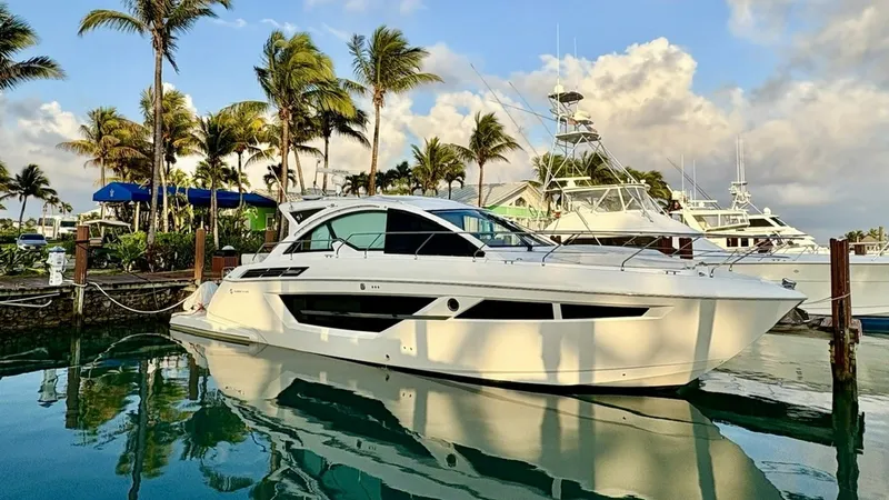 Slide: The Image of Side Profile in Marina Setting The 2023 Cruisers Yachts 50 Cantius, known as 'Past Time,' is elegantly docked against a picturesque marina backdrop. This side profile showcases its sleek, modern lines and expansive windows, offering a glimpse into the luxurious interiors. The yacht's p - 6510170