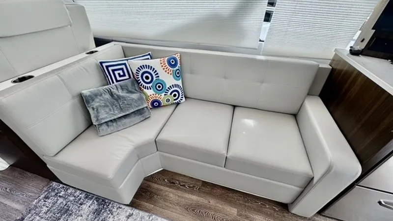 Slide: The Image of Salon Seating Area with Modern Sofa This inviting salon features a sleek, L-shaped sofa upholstered in soft, light-toned fabric, complemented by decorative throw pillows. The contemporary design offers comfort and style, with ample natural light filtering through the large windows. The eleg - 6489137