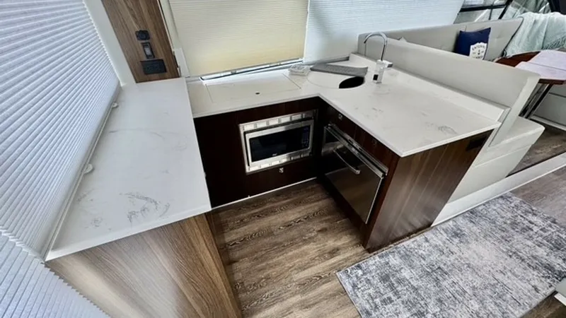 Slide: The Image of Galley with Modern Appliances This well-appointed galley on the 2023 Cruisers Yachts 50 Cantius features sleek countertops and high-end appliances, including a built-in microwave and oven. The contemporary wood cabinetry complements the sophisticated flooring, creating a stylish and f - 6489141