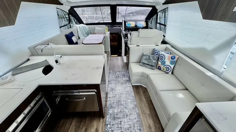 Slide: The Image of Interior Salon and Helm View The luxurious interior salon of the 2023 Cruisers Yachts 50 Cantius offers a spacious and modern layout featuring elegant white leather seating and a stylish galley with sleek countertops. Large windows provide abundant natural light, enhancing the airy a - 6489139
