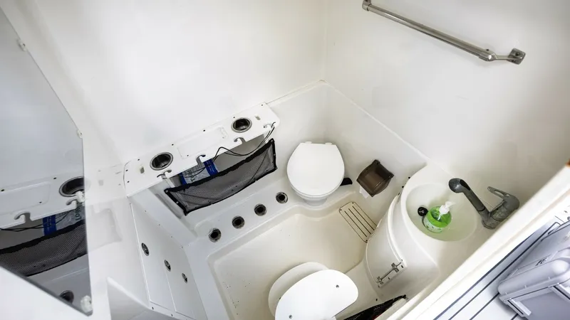 Slide: The Image of Compact Marine Head Compartment This image showcases the compact and efficient marine head compartment of the 2005 Triton 351 Center Console. The space features a practical layout with a marine toilet, sink, and essential storage options. The clean, white finish and stainless steel fixt - 6687489