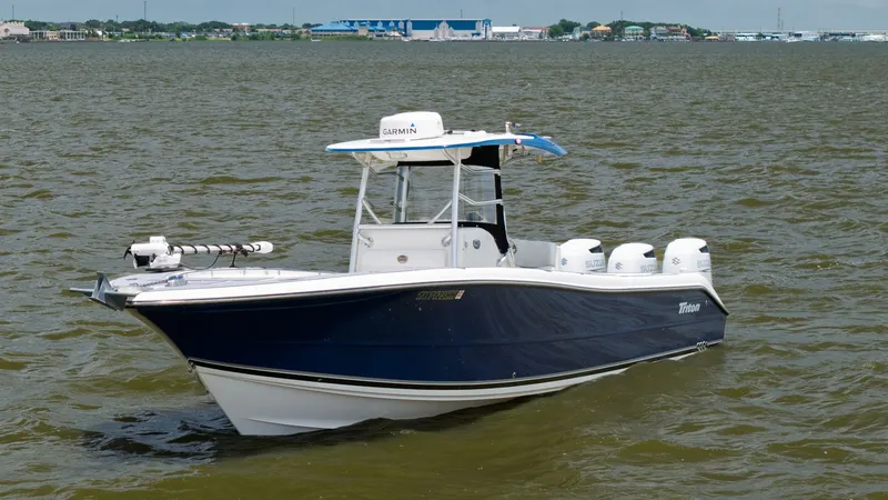 Slide: The Image of Triton 351 Center Console Exterior View This 2005 Triton 351 Center Console showcases a sleek, dark hull with a sharp, aerodynamic design. The vessel is equipped with powerful triple outboard engines, ensuring robust performance on the water. The center console is topped with a T-top for shade - 6687490
