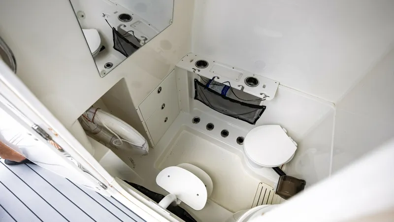 Slide: The Image of Compact Head Compartment Interior This image showcases the compact head compartment of the 2005 Triton 351 Center Console. The space is efficiently designed with a marine toilet and a small basin, complemented by a mirror for added functionality. The white finish and practical storage sol - 6687488