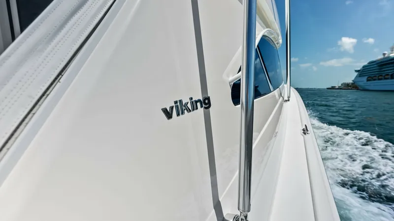 Slide: The Image of Portside Exterior with Viking Logo This image showcases the sleek portside exterior of the 2018 Viking 62 Convertible, featuring the iconic Viking logo. The smooth, clean lines of the hull highlight the craftsmanship and attention to detail synonymous with Viking yachts. The view captures - 8440085