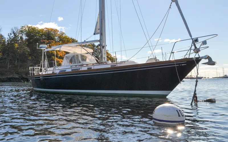 Slide: The Image of 1984 Bristol 41.1 | Petrel Sailboat anchored on calm water near a wooded shoreline. - 6523151