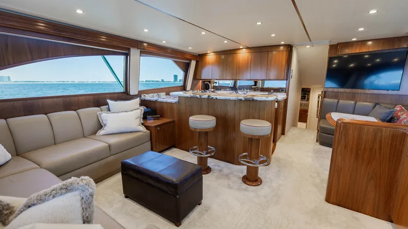 Slide: The Image of Spacious Salon with Galley View This elegant salon on the Viking 62 Convertible showcases a luxurious open layout with plush seating and rich wood finishes. Large windows provide expansive views, enhancing the bright and airy atmosphere. The adjoining galley features a sleek countertop - 6711664