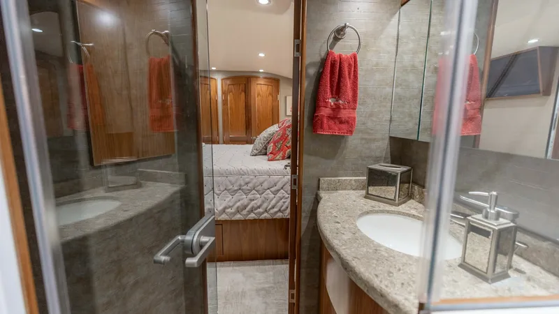 Slide: The Image of Luxury Ensuite Bathroom and Stateroom This image showcases the elegant ensuite bathroom of the 2020 Viking 62 Convertible. The space features a sleek, curved vanity with a polished stone countertop and modern fixtures. The adjoining stateroom is visible, highlighting luxurious bedding and war - 6711682