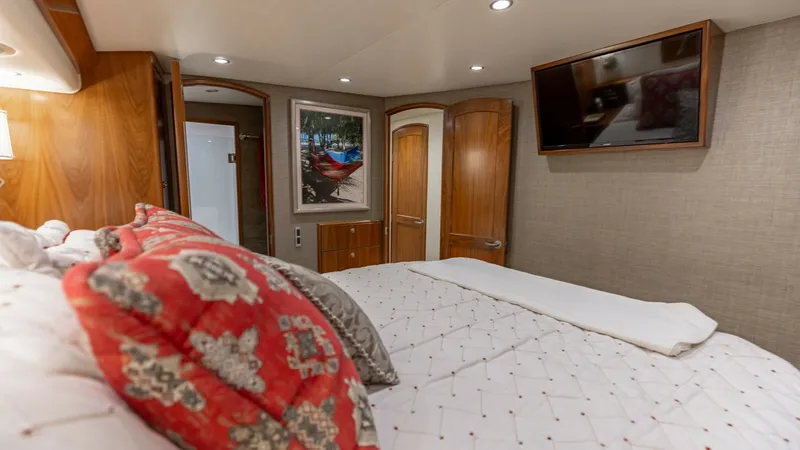 Slide: The Image of Luxurious Master Stateroom Interior The master stateroom of the 2020 Viking 62 Convertible exudes comfort and elegance. It features a plush, king-sized bed adorned with patterned pillows and a quilted bedspread, complemented by warm wood finishes and ambient lighting. A mounted flat-screen - 6711677