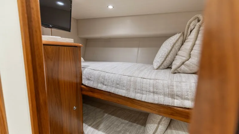 Slide: The Image of Cozy Twin Bunk Cabin View This inviting cabin on the 2020 Viking 62 Convertible features neatly arranged twin bunks, ideal for comfortable overnight stays. The warm wood finishes and soft lighting create a relaxing atmosphere. A compact flat-screen TV adds entertainment options, e - 6711687