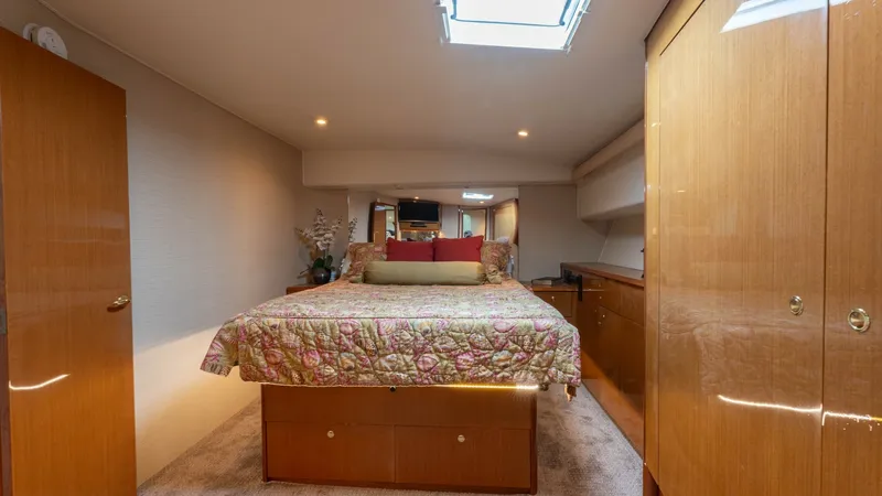 Slide: The Image of Master Stateroom with Skylight The master stateroom of the Viking 65 Enclosed Bridge features a luxurious queen-sized bed adorned with elegant bedding. A skylight above the bed floods the room with natural light, enhancing the warm ambiance created by the wood finishes and soft carpeti - 6767180