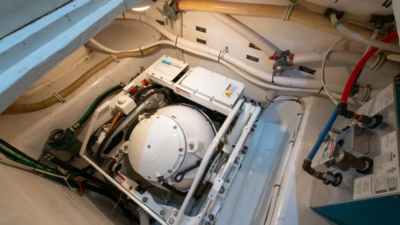 Slide: The Image of Engine Room with Generator This image showcases the engine room of the Viking 65 Enclosed Bridge, featuring a well-maintained generator. The space is efficiently organized, with neatly arranged piping and wiring, ensuring optimal functionality. The clean, white surfaces reflect the - 6767184