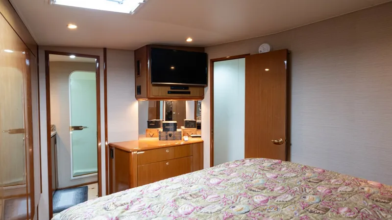 Slide: The Image of Master Stateroom with Ensuite Access The master stateroom offers a cozy and inviting space with warm wood finishes and soft overhead lighting. A large bed with a floral-patterned coverlet dominates the room, complemented by a built-in entertainment center and ample storage. Convenient access - 6767181