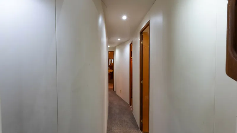 Slide: The Image of Upper Deck Interior Hallway This sleek hallway on the Viking 65 Enclosed Bridge yacht features soft, recessed lighting that enhances the clean, modern lines of the walls. The corridor is elegantly carpeted, leading to various compartments, offering both functionality and aesthetic a - 6767170